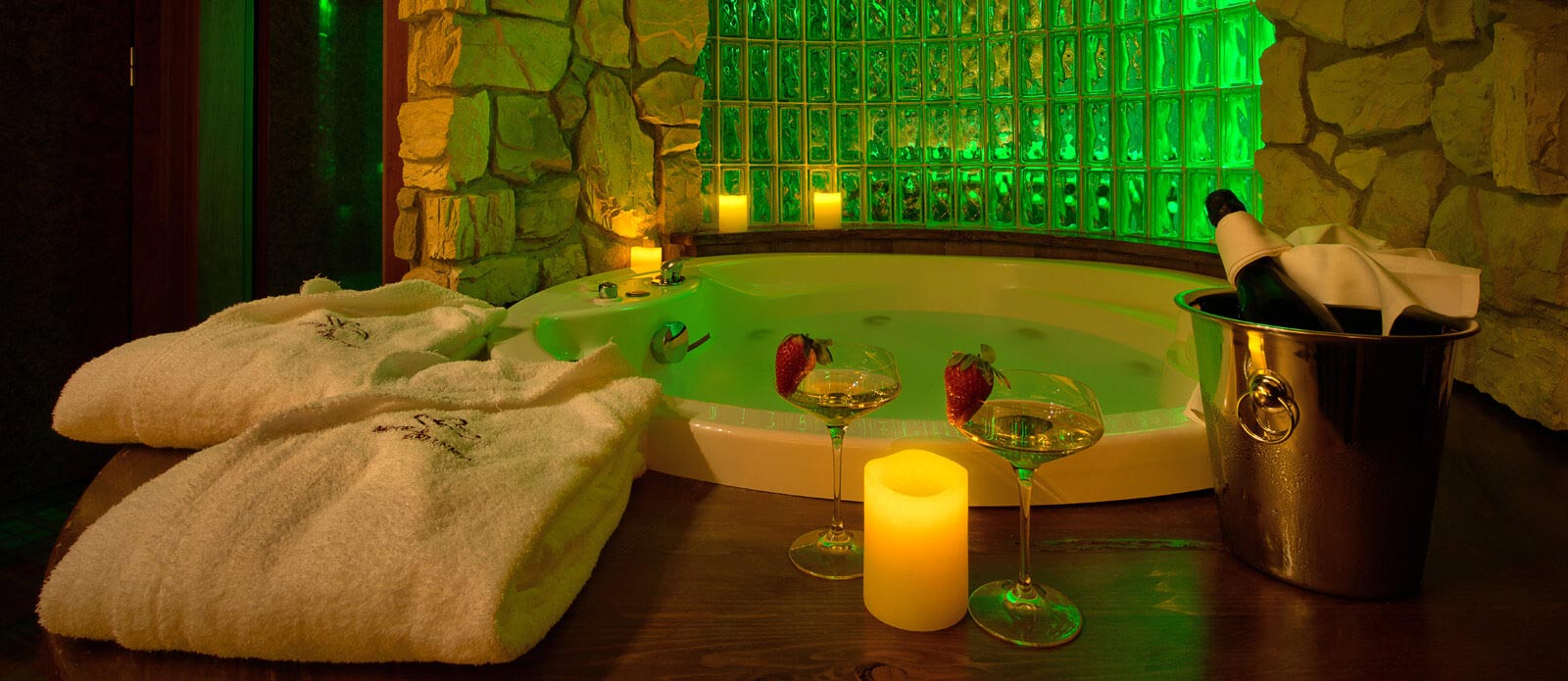 Motel K Senior Suite Baita  Motel K Senior Suite Baita vista su vasca idromassaggio rotonda per 2 persone, con servizio candele in suite, bottiglia di champagne in secchiello del ghiaccio e 2 bicchieri appoggiati a bordo vasca camera a tema Chalet di montagna