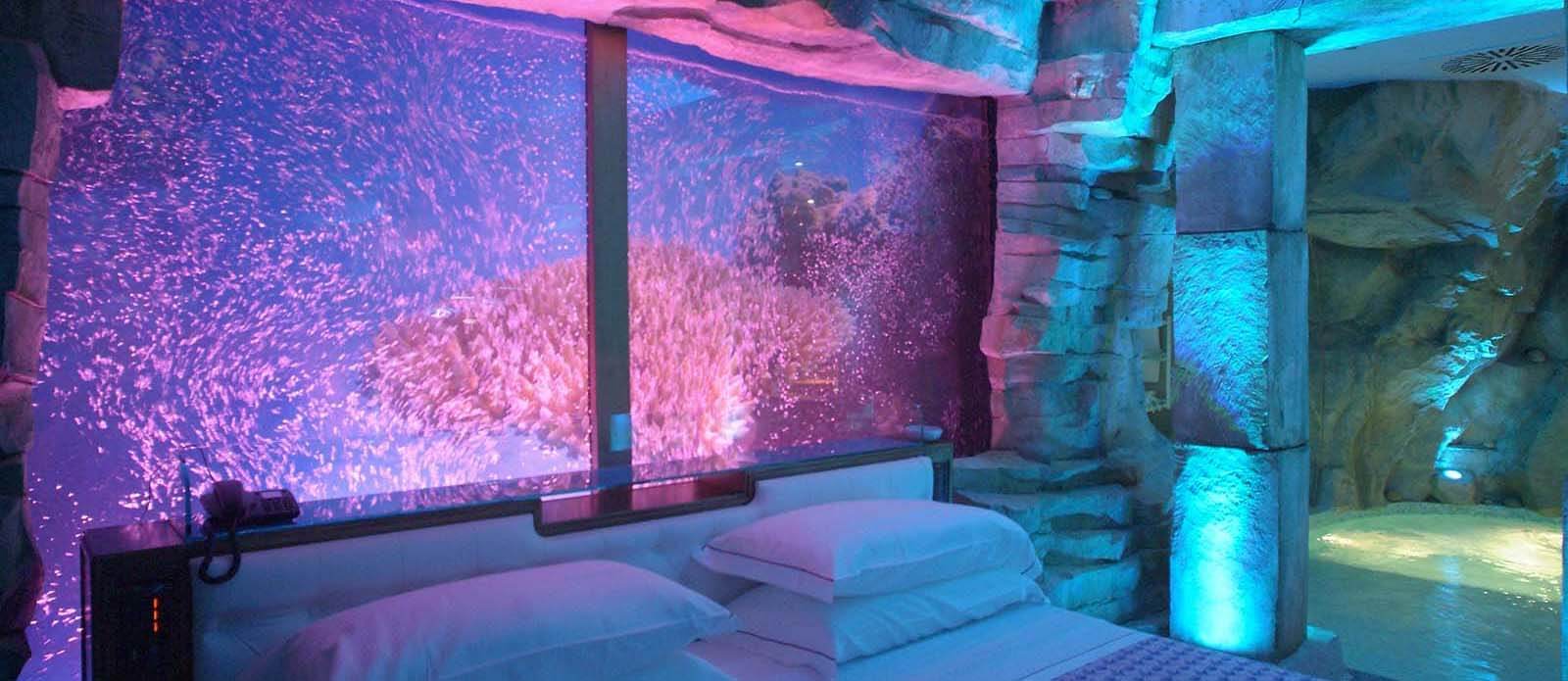 Motel K Wellness Suite Atlantide Motel K Wellness Suite Atlantide vista sul letto matrimoniale con vero acquario con cromoterapia dietro al letto, in sfondo si intravede la mini piscina idromassaggio camera a tema isola Atlantide