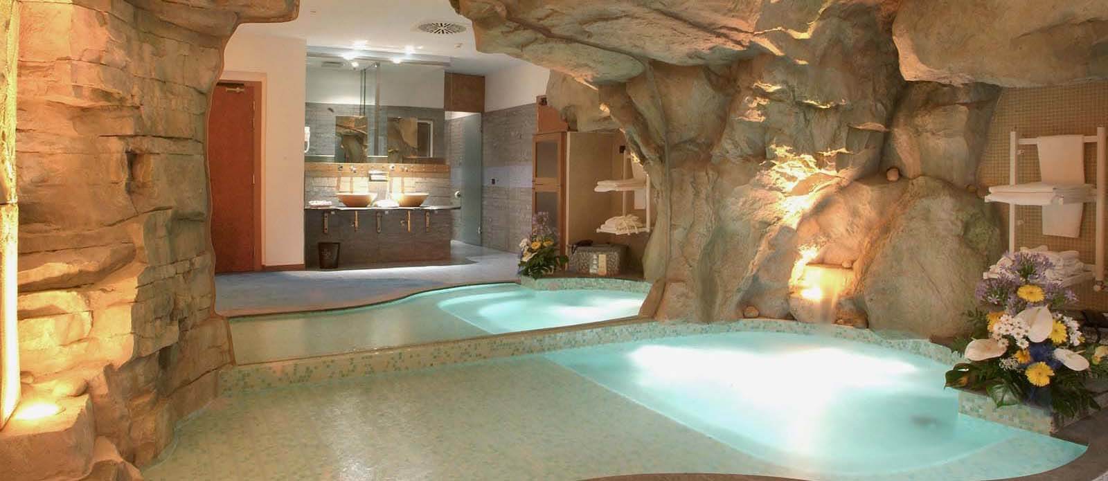 Motel K Welleness Suite Atlantide Motel K Welleness Suite Atlantide vista sulla mini piscina idromassaggio con cascata e cromoterapia a sfioro col pavimento della camera, un grosso specchio di fianco alla mini piscina riflette sui servizi igienici, camera a tema isola Atlantide