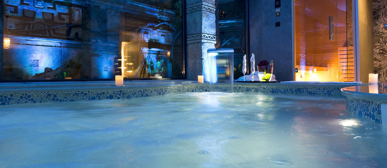 Motel K Wellness Suite Tempio Perduto Motel K Wellness Suite Tempio Perduto vista sulla mini piscina idromassaggio con cascata, servizio candele in suite, bottiglia di champagne in secchiello del ghiaccio a bordo piscina, si intravede la sauna finlandese nello sfondo, camera a tema atlantide